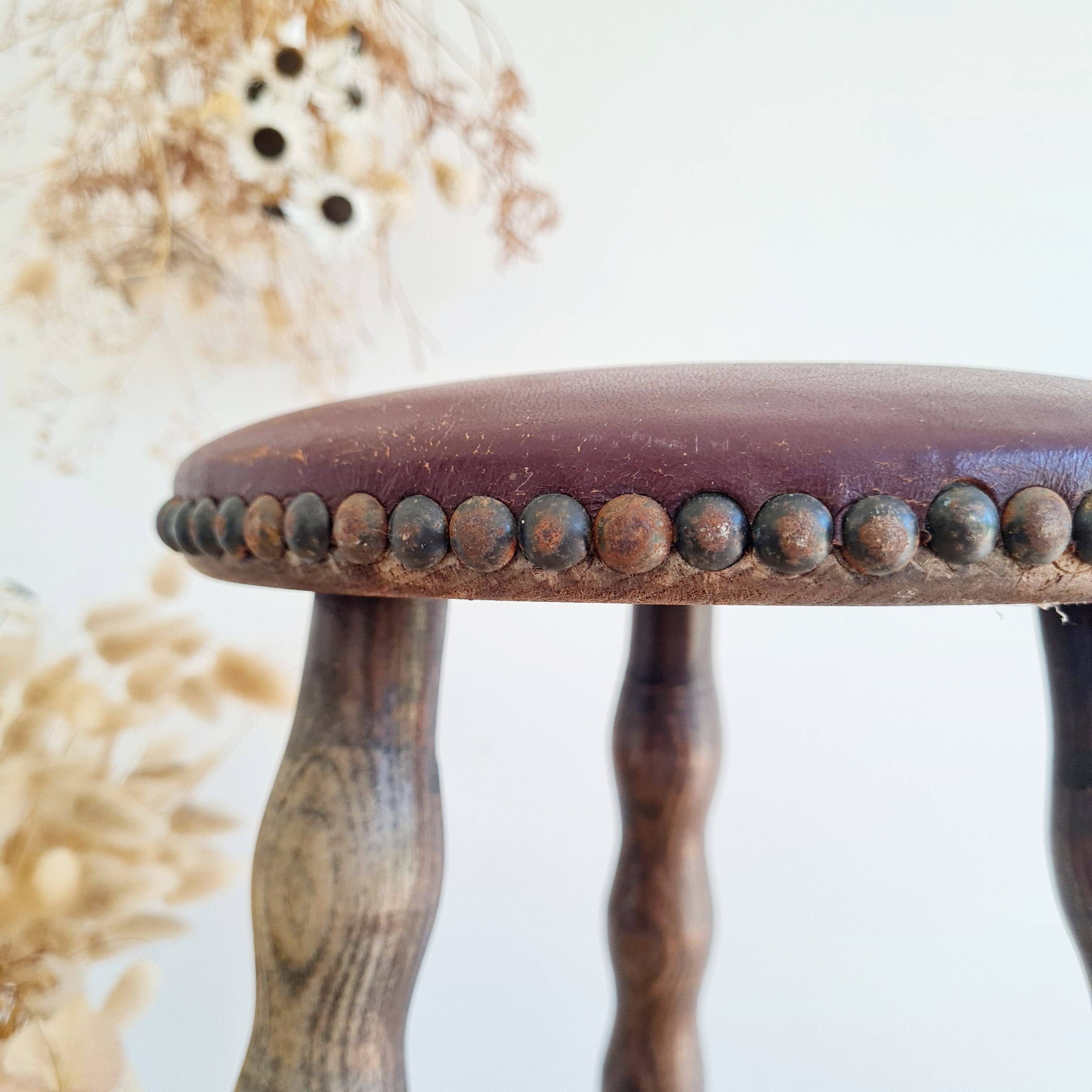 Antique tripod stool with turned wooden legs and leather seat.