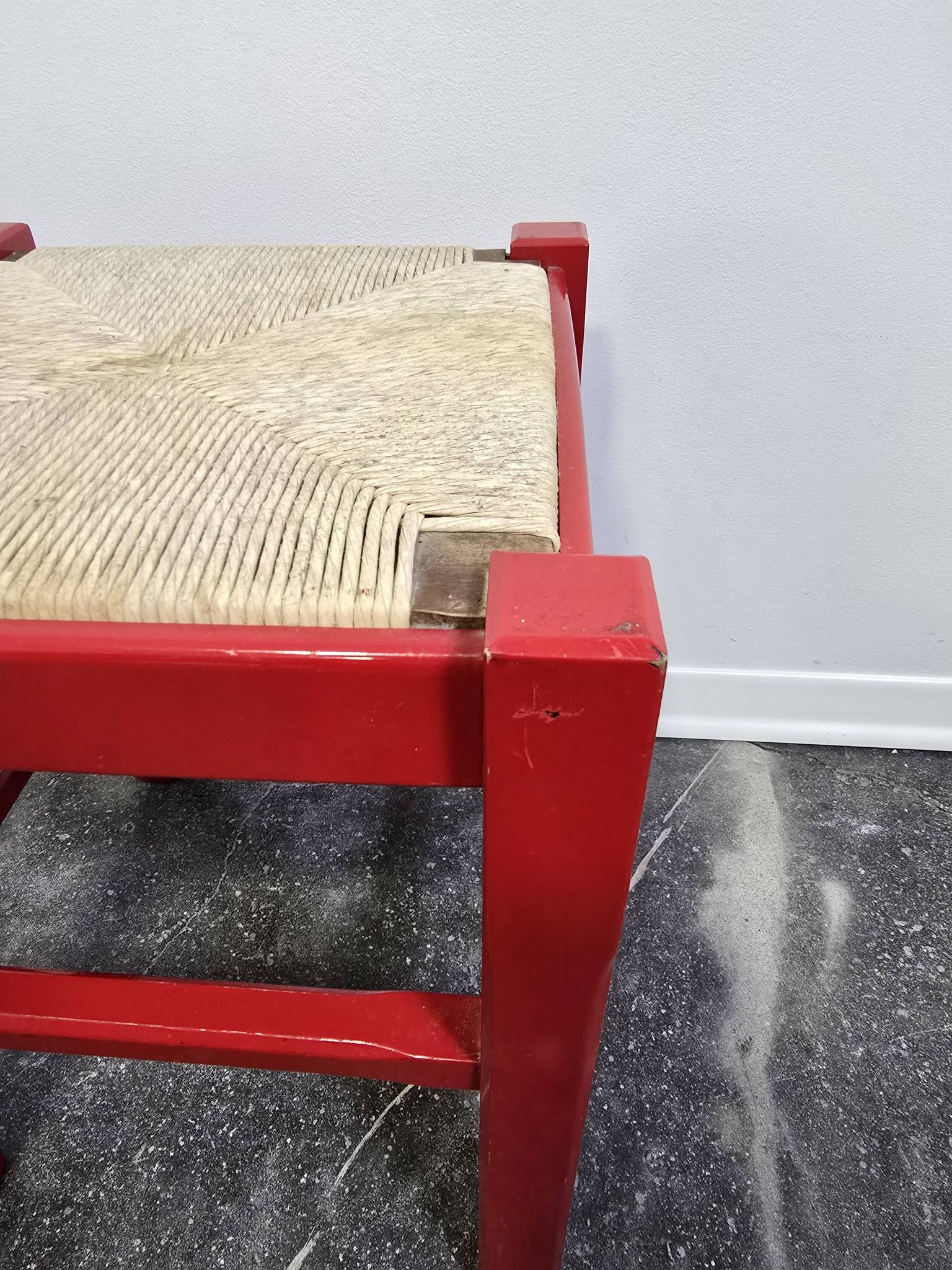 Red wooden stool with a woven straw seat.