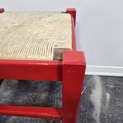 Red wooden stool with a woven straw seat.