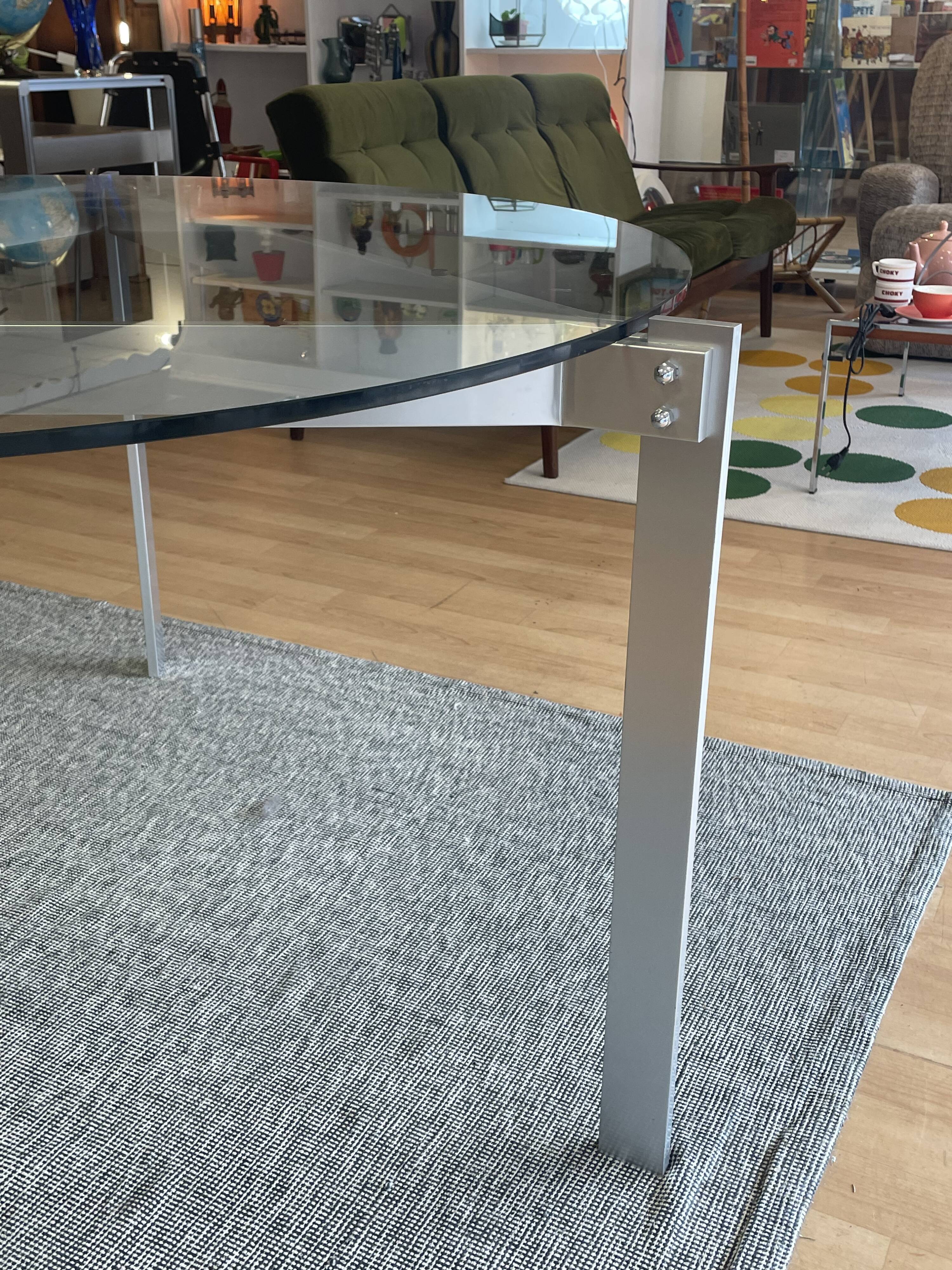 Round dining table with a glass top and brushed metal triangular frame.