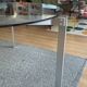 Round dining table with a glass top and brushed metal triangular frame.
