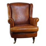 Subtle sheepskin wing chair in good condition on brass front wheels