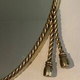 Oval brass mirror surrounded by a cord.