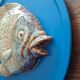 Vallauris ceramic wall sculpture of a relief fish on a blue plaque.