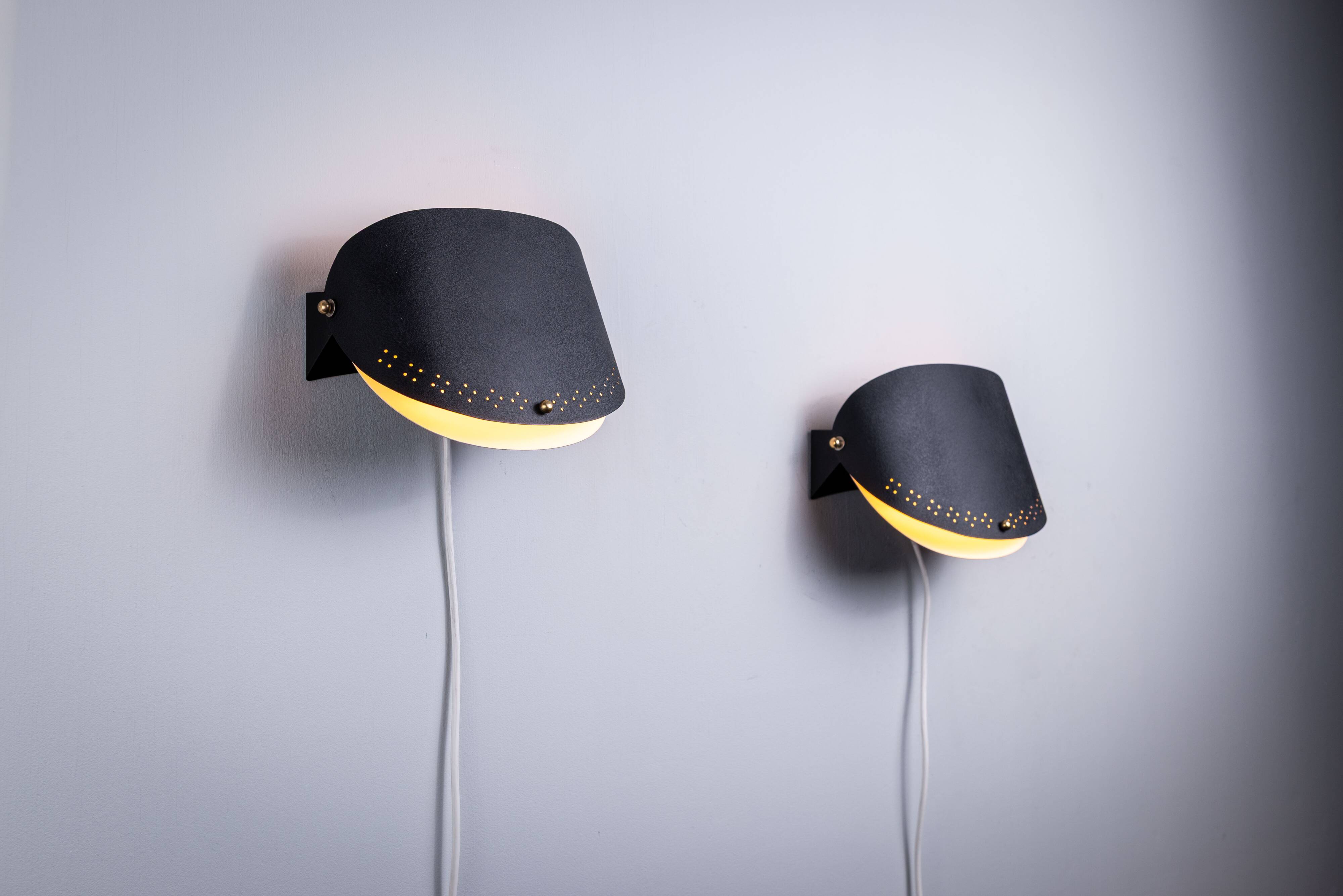 Matte black wall lamps with perforated shades and brass details
