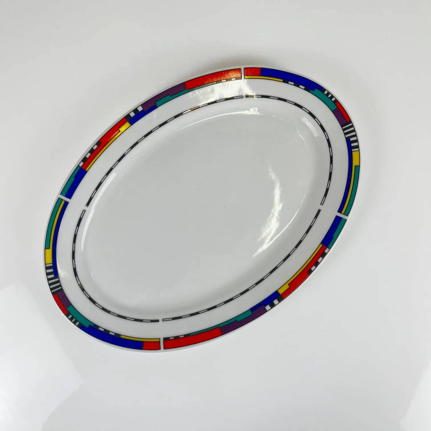 Oval porcelain plate by Van Well, multicoloured geometric border, 1980.
