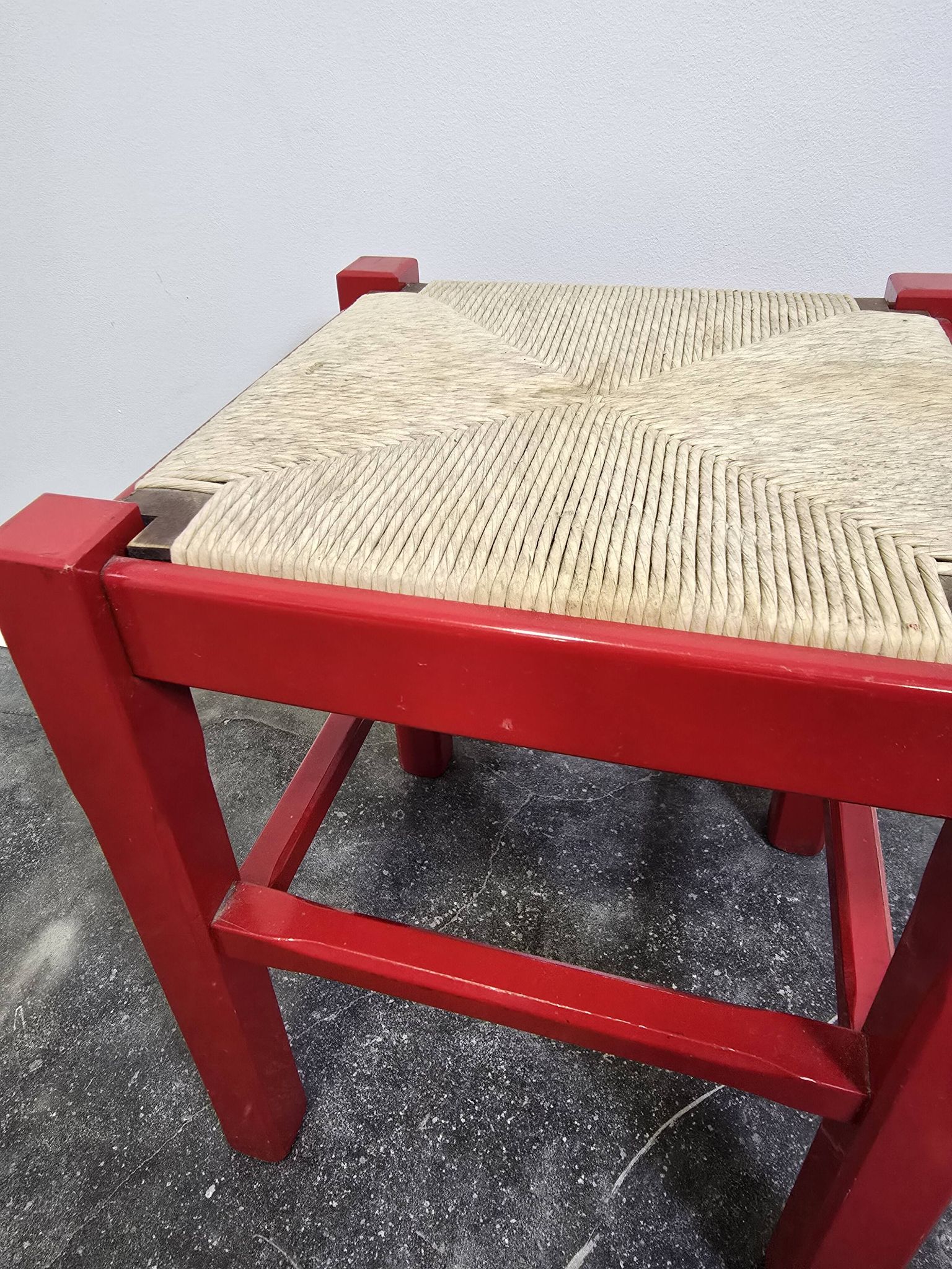 Red wooden stool with a woven straw seat.