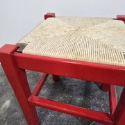 Red wooden stool with a woven straw seat.