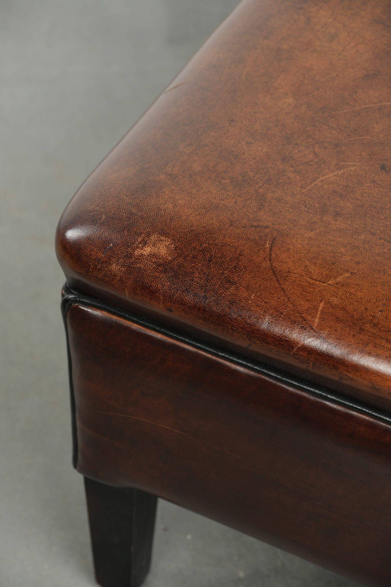 Pouf carré marron foncé en peau de mouton avec un passepoil noir.
