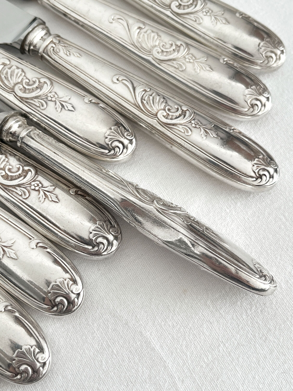 12 antique silver-plated knives with acanthus shell decoration and stainless steel blades.