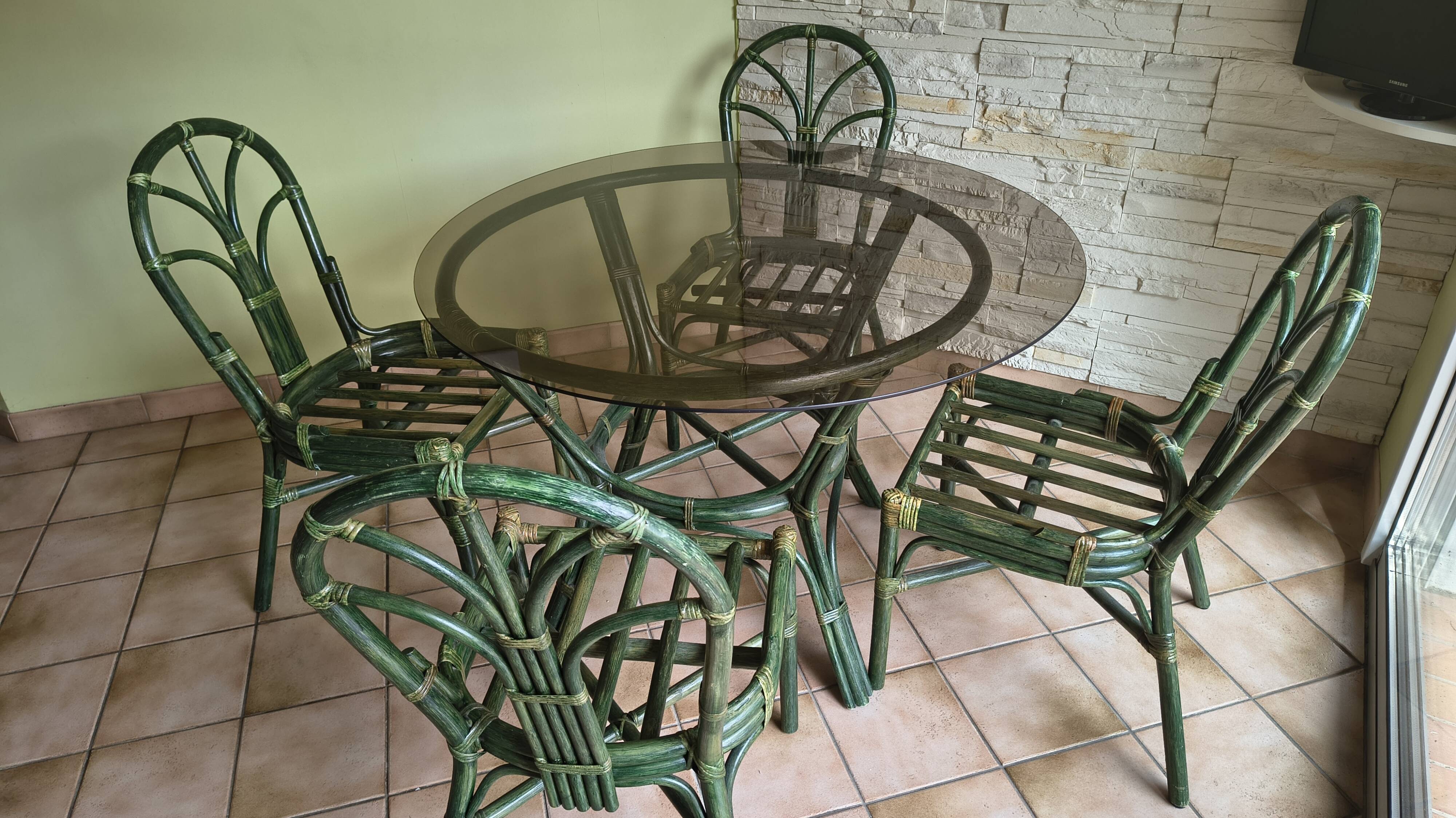 Round rattan table with glass top and 4 green rattan chairs.