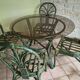 Round rattan table with glass top and 4 green rattan chairs.