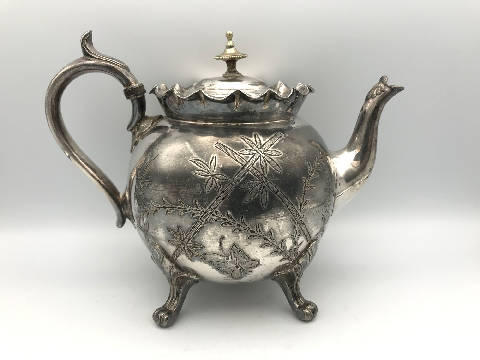 Old teapot pourer in silver metal decorated with foliage and butterflies
