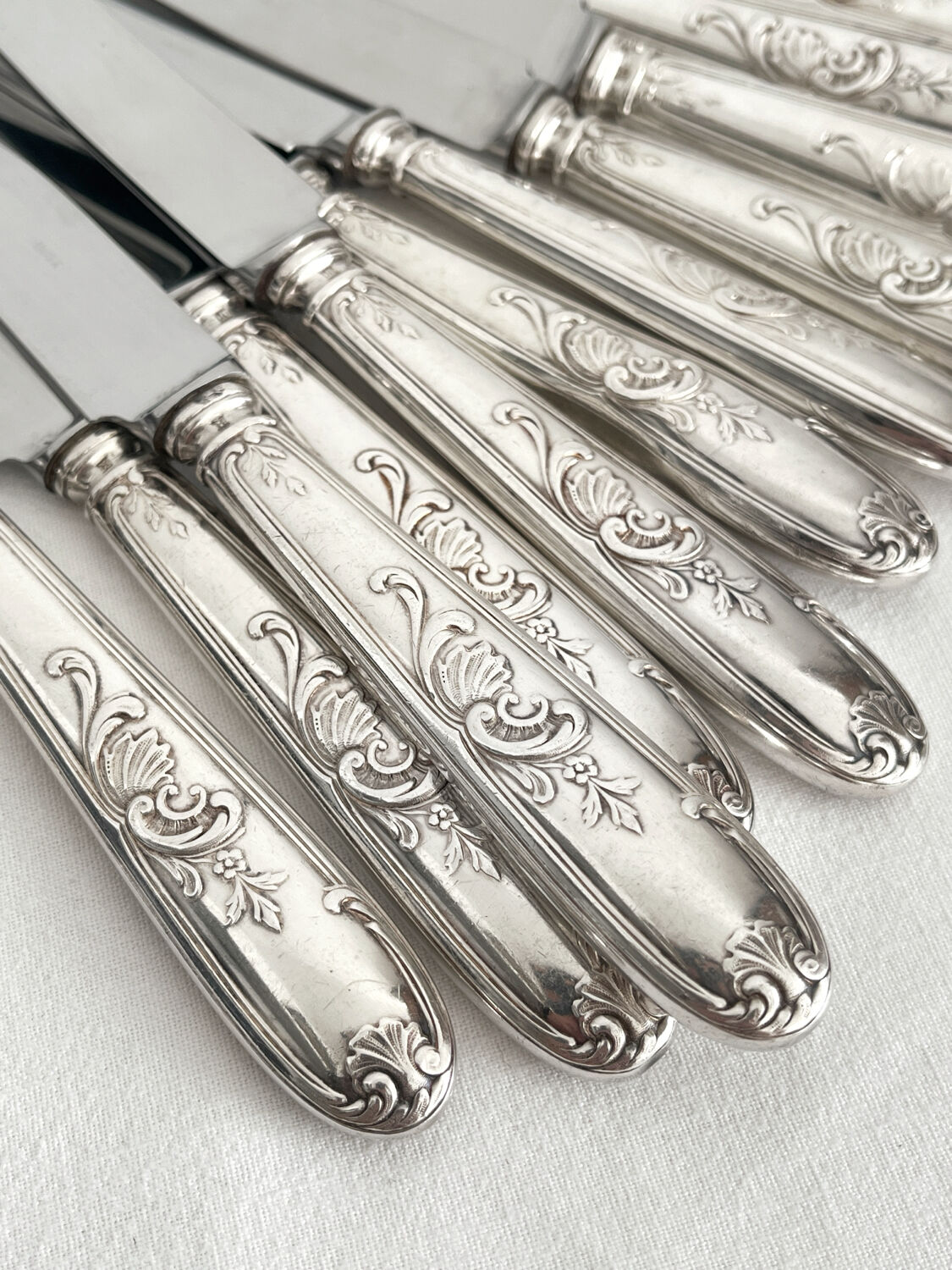 12 antique silver-plated knives with acanthus shell decoration and stainless steel blades.