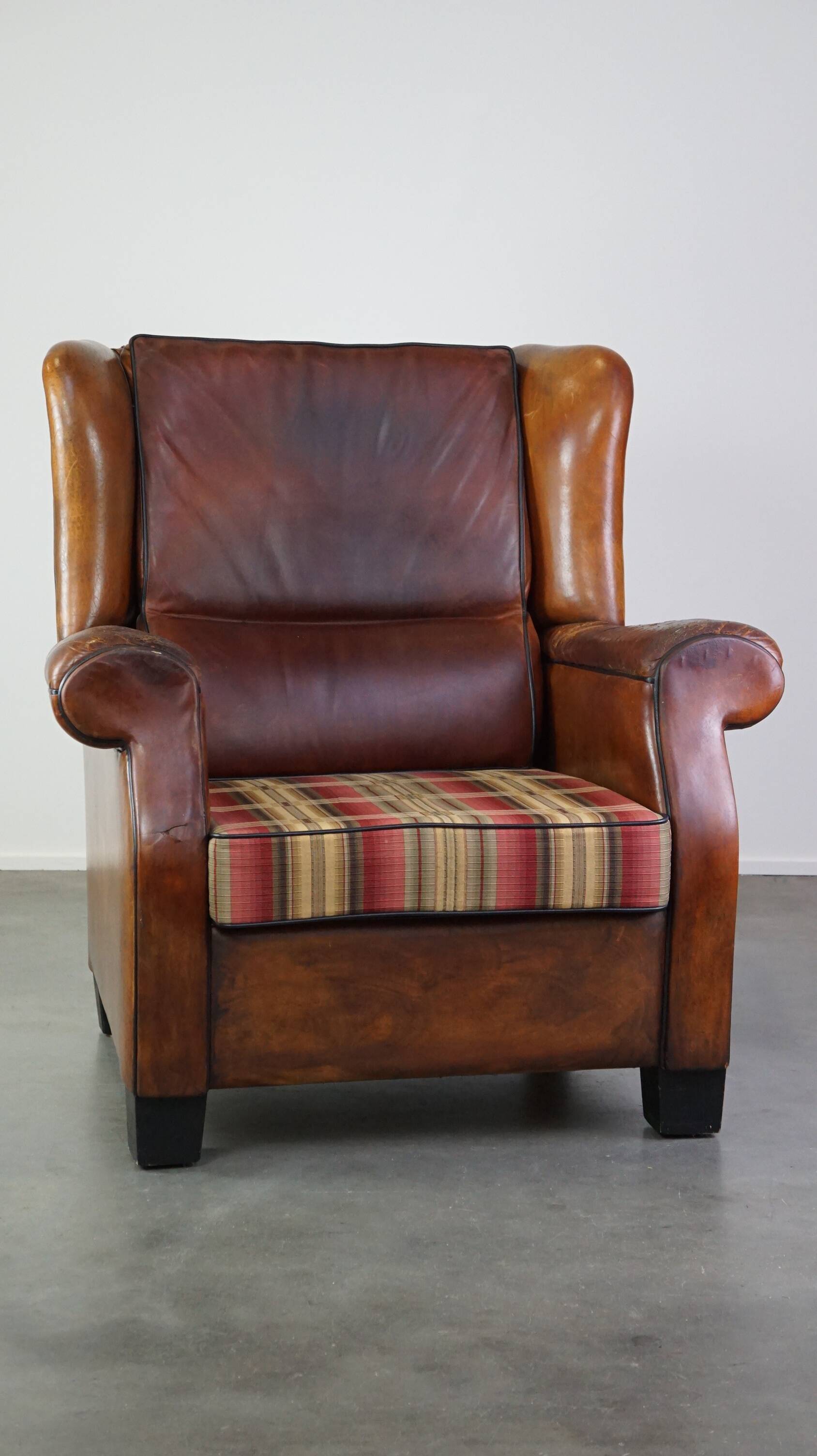 Very large worn sheepskin wing chair with a checked seat cushion