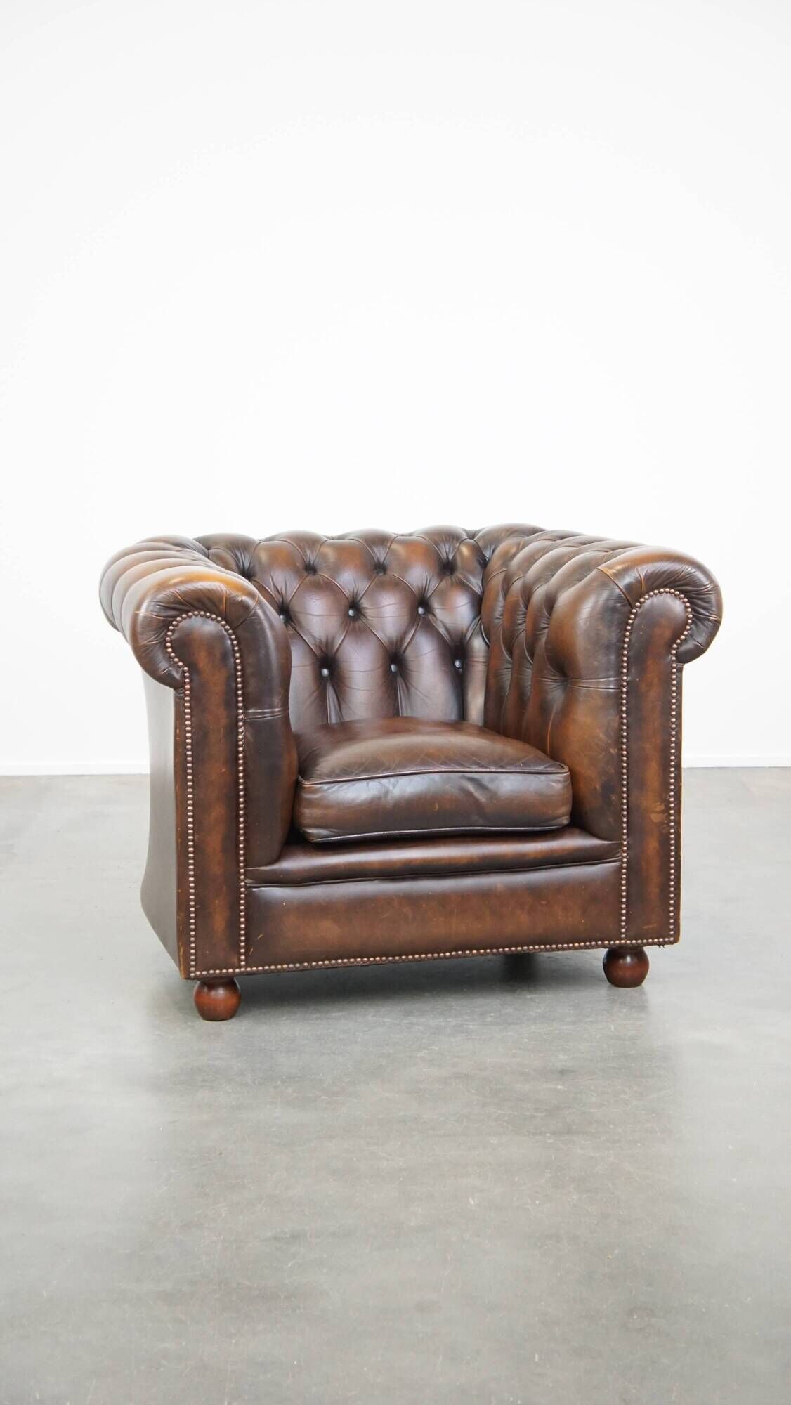 Cowhide English Chesterfield armchair with ball legs and timeless finish
