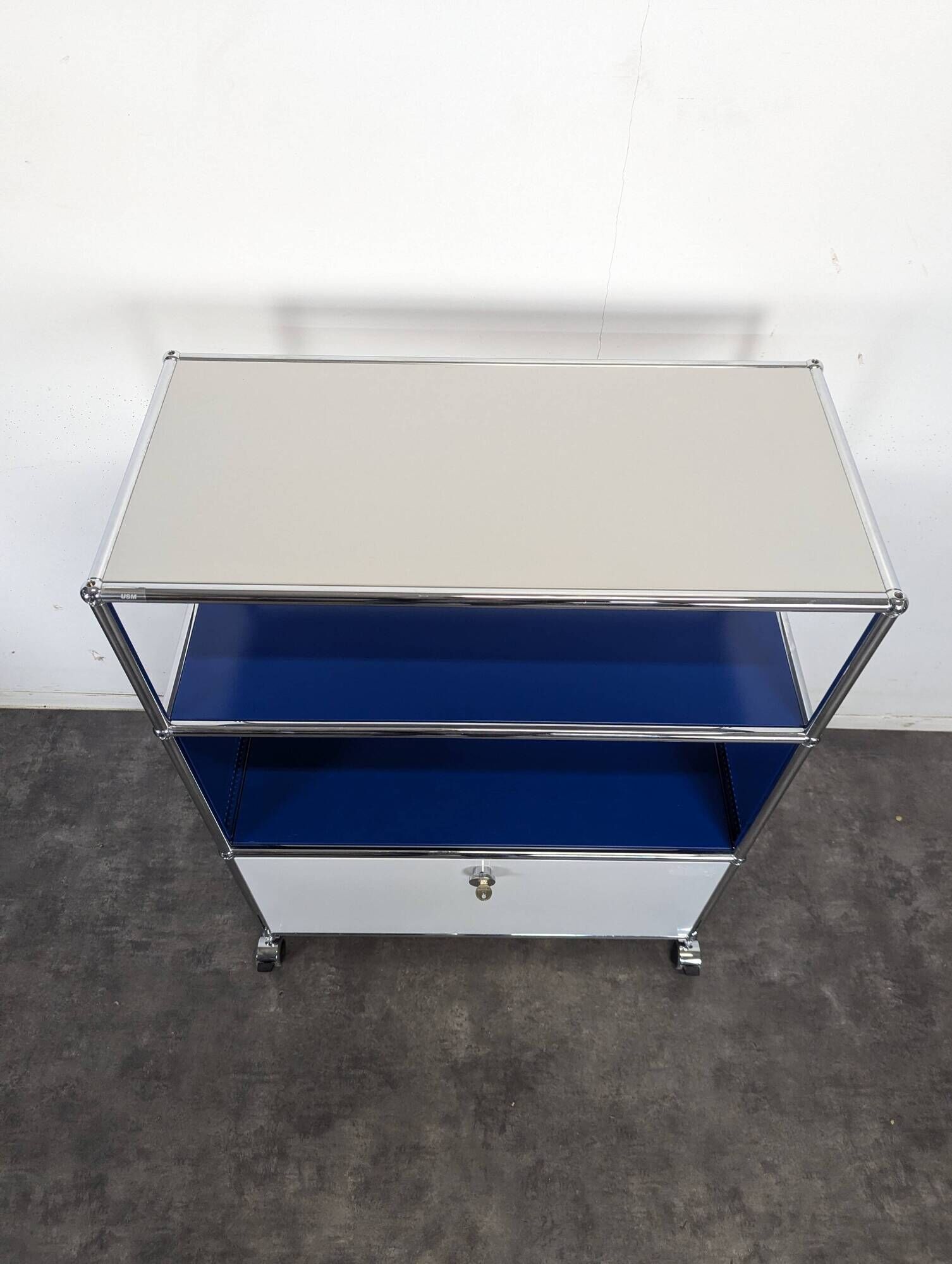 USM Haller furniture in gentian blue and white with a drop-down door on wheels.