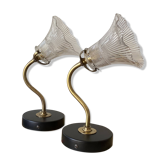 Pair of brass swan neck wall lights with transparent glass shades.