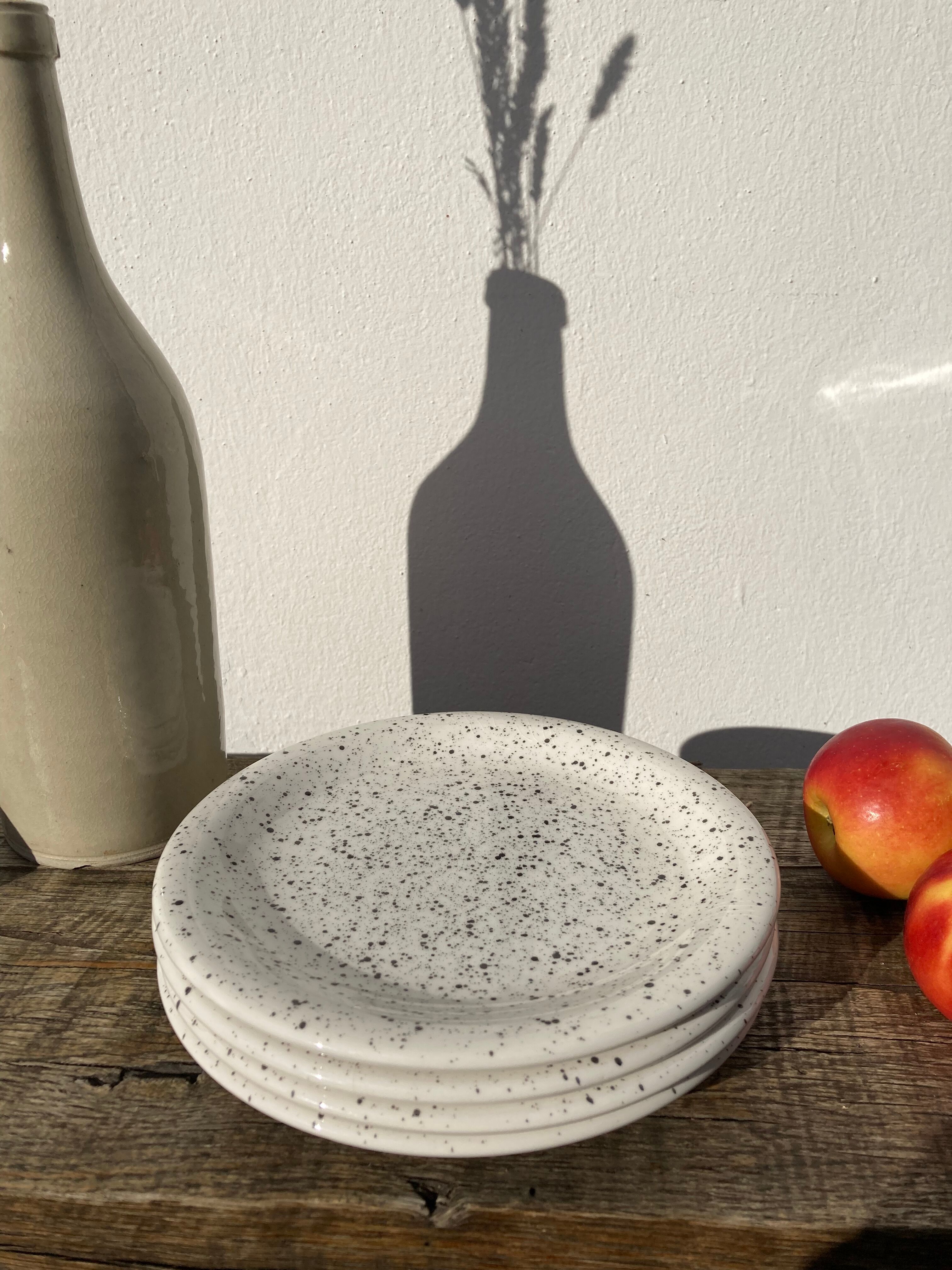 4 black speckled dessert plates on a vintage white background