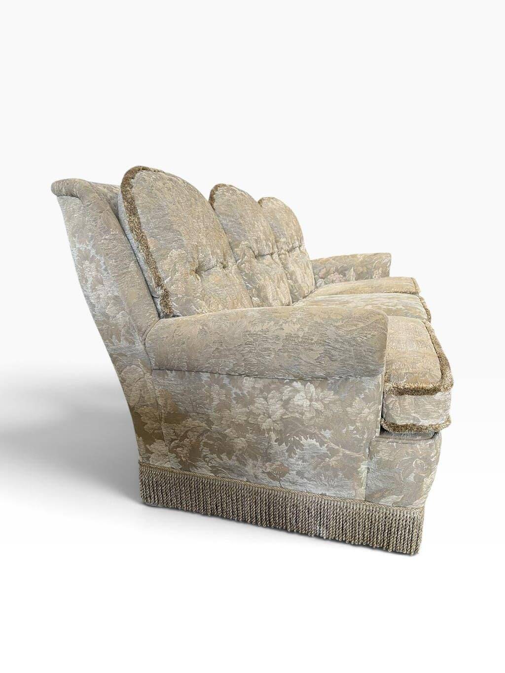 Vintage beige three-seater sofa with floral pattern and fringes.