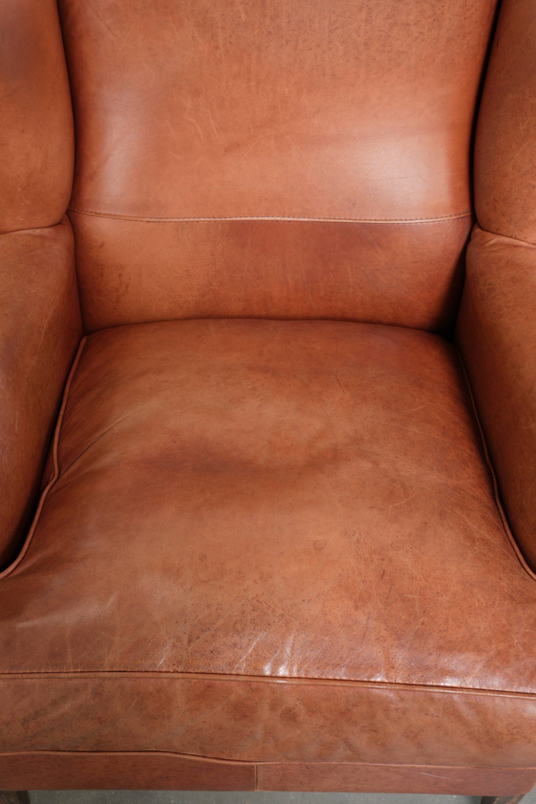 Light cognac-coloured cow leather wingback armchair with matching piping