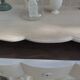 A beautifully crafted crossbow-shaped chest of drawers, finished in pearl grey with a whitewashed top.