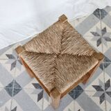 Vintage low stool in rustic style made of wood with a straw seat.
