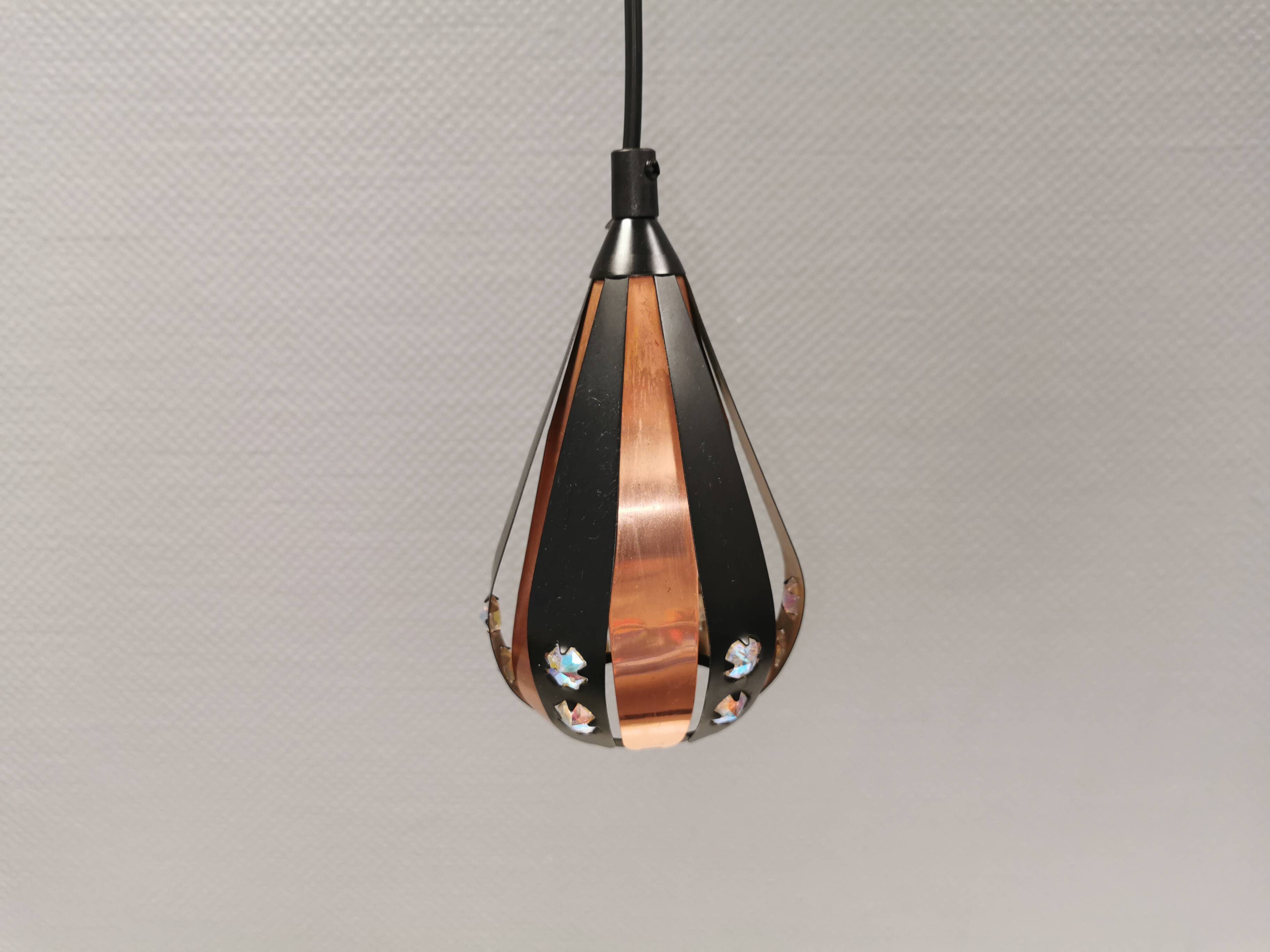 A teardrop-shaped pendant lamp made of copper, black metal, and prisms.