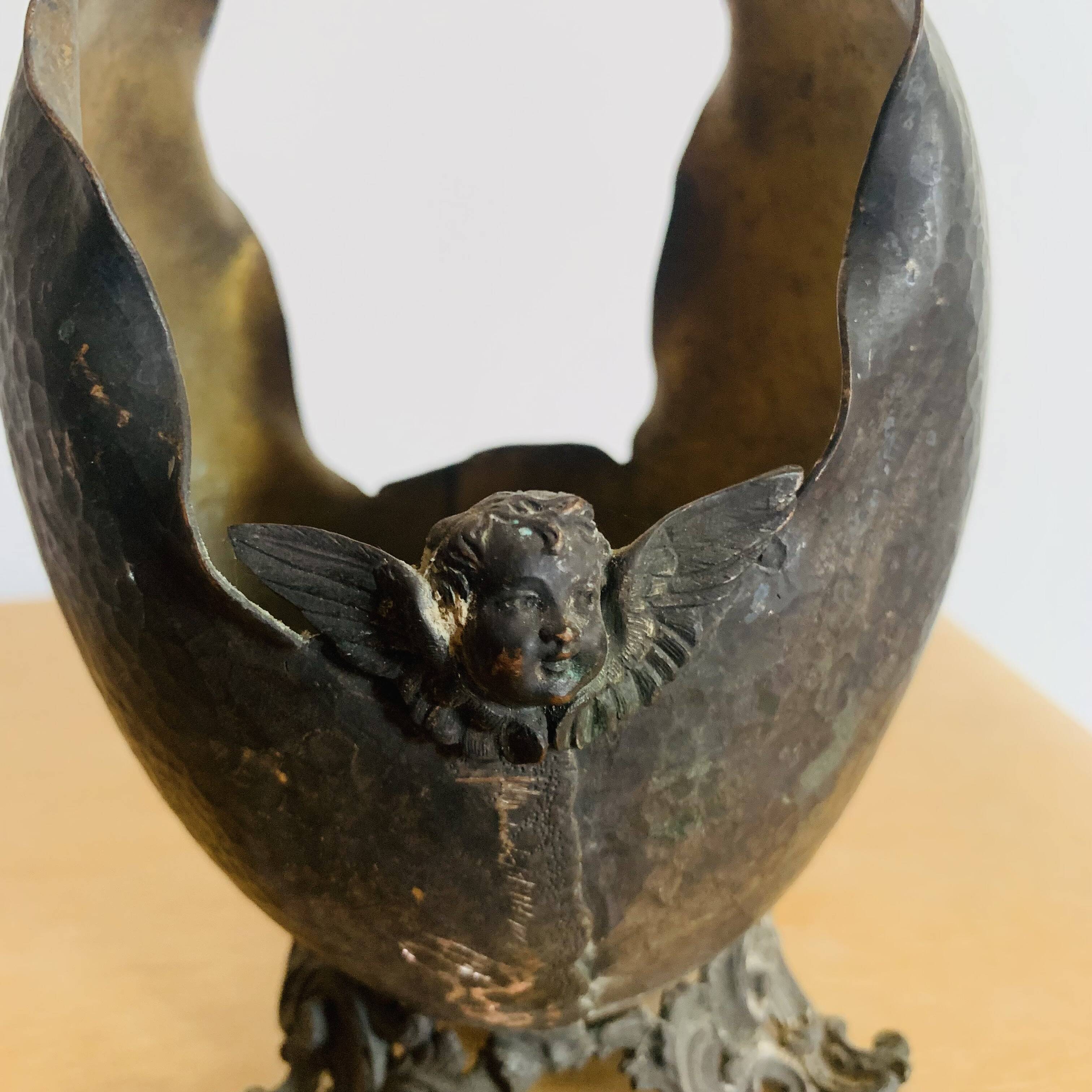 Antique decorative cup in hammered metal with putto design.