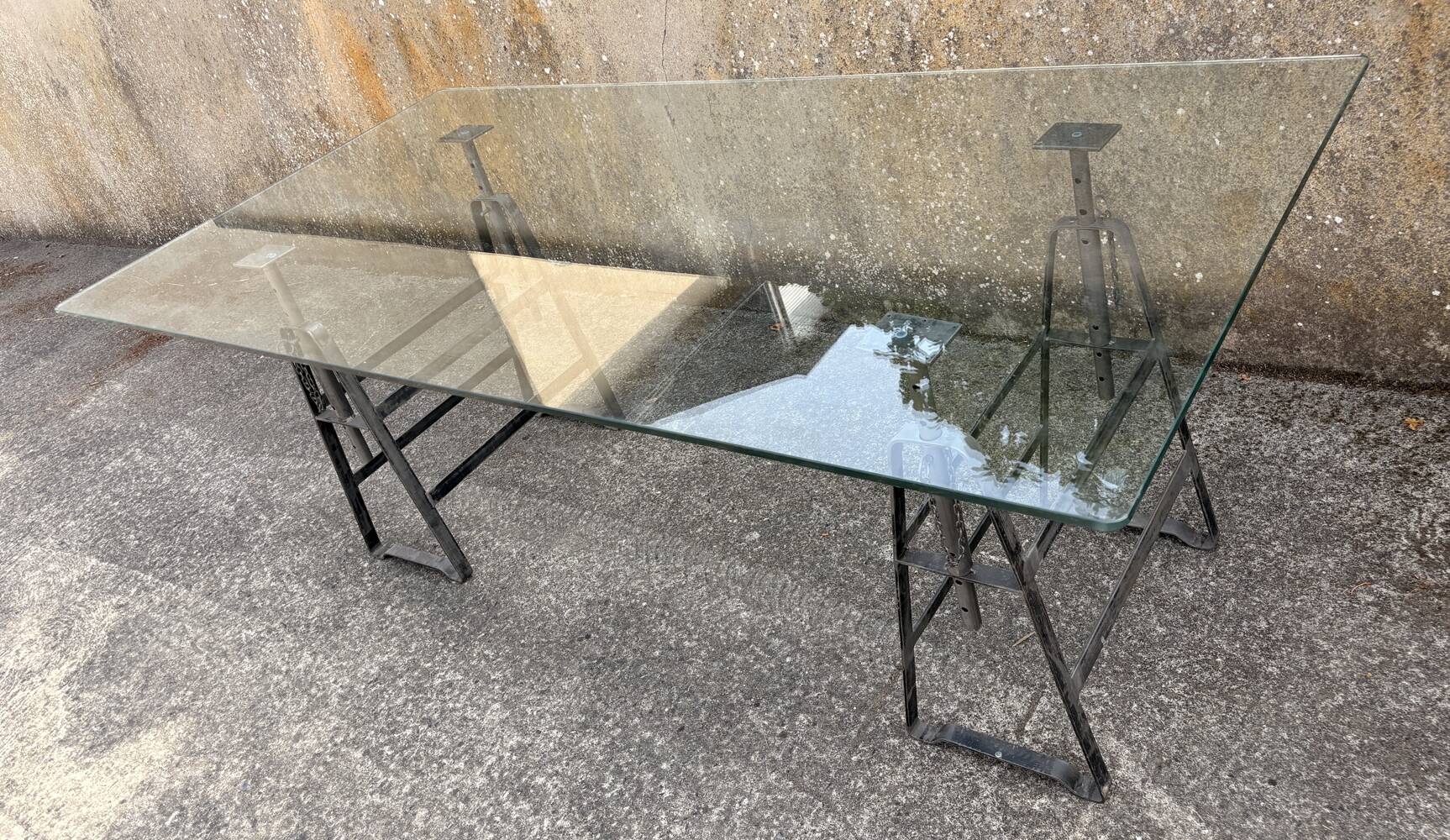 Large vintage industrial glass table with adjustable metal trestles.
