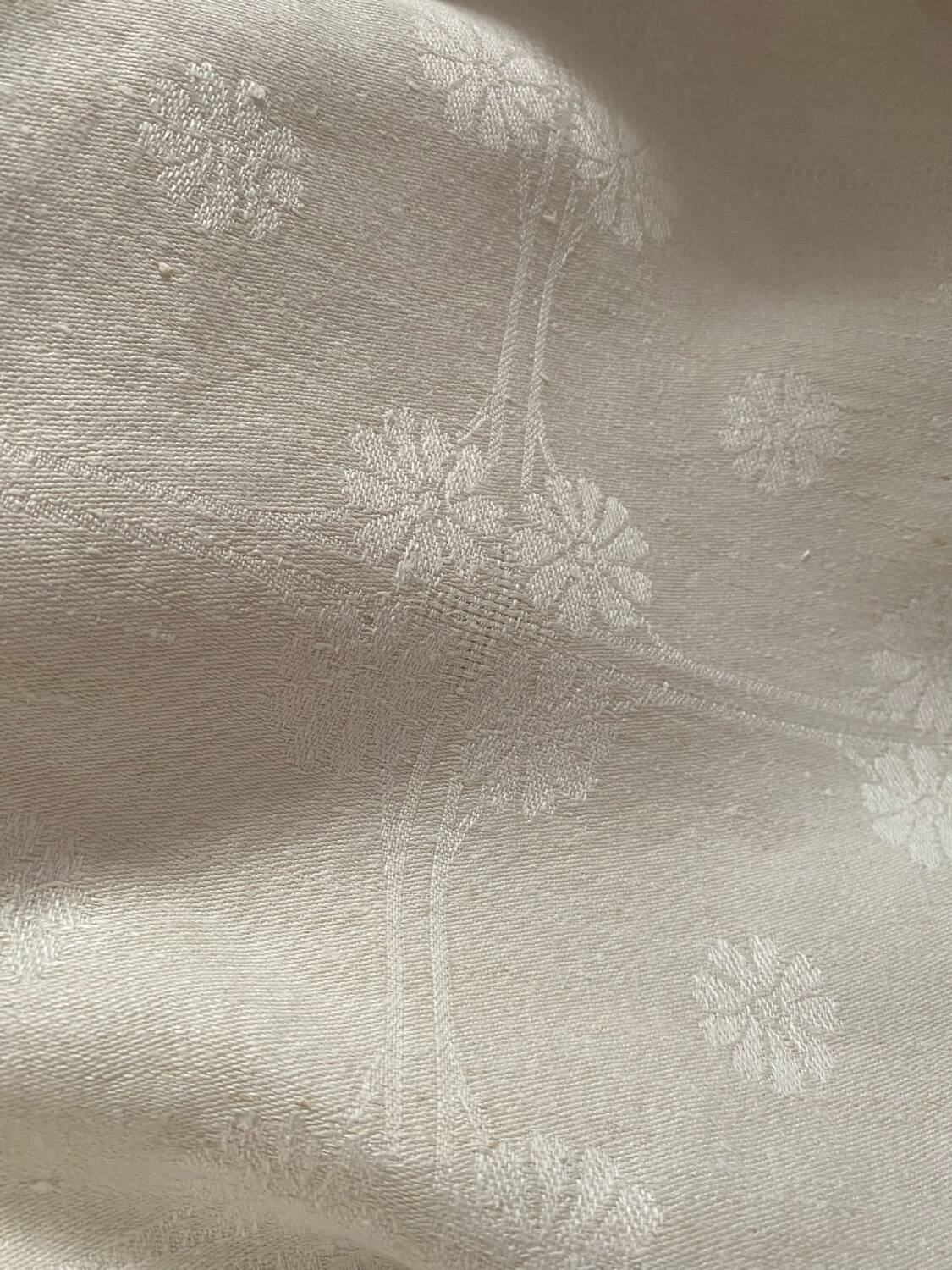 Damask tablecloth with a floral pattern and a central embroidered monogram.