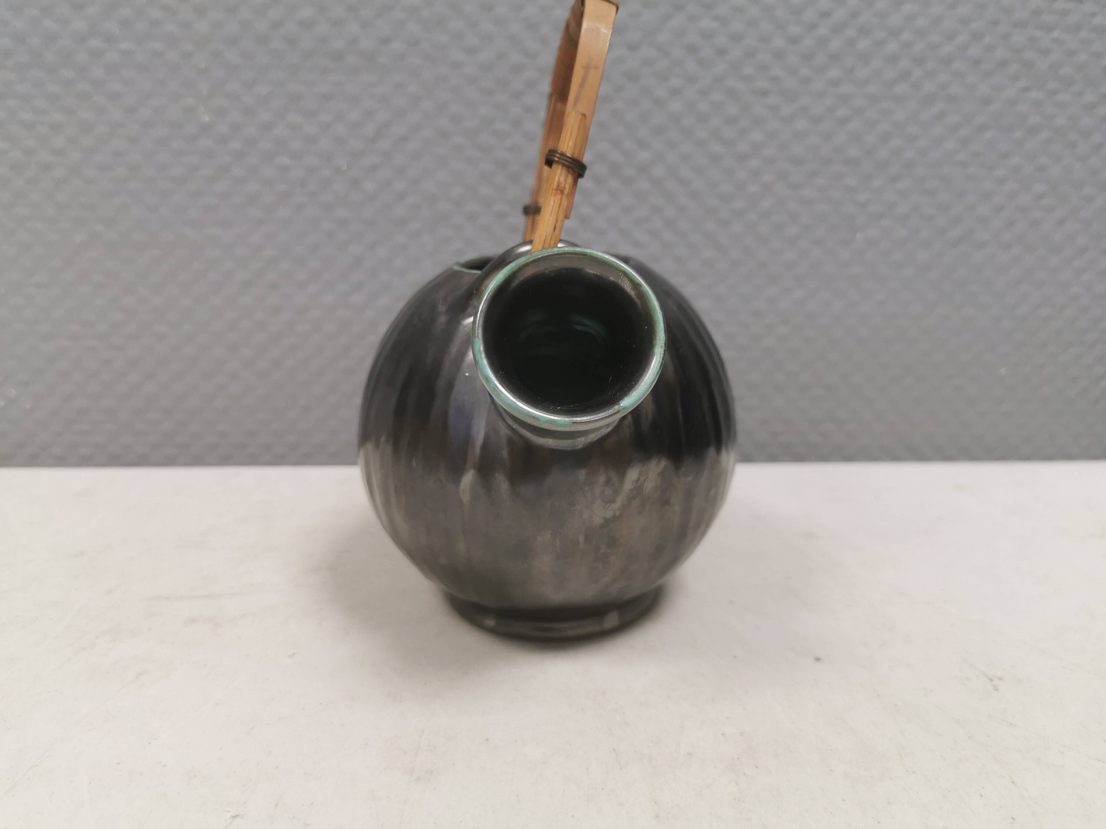 A ceramic jug with a metallic glaze and a handle made of woven raffia.