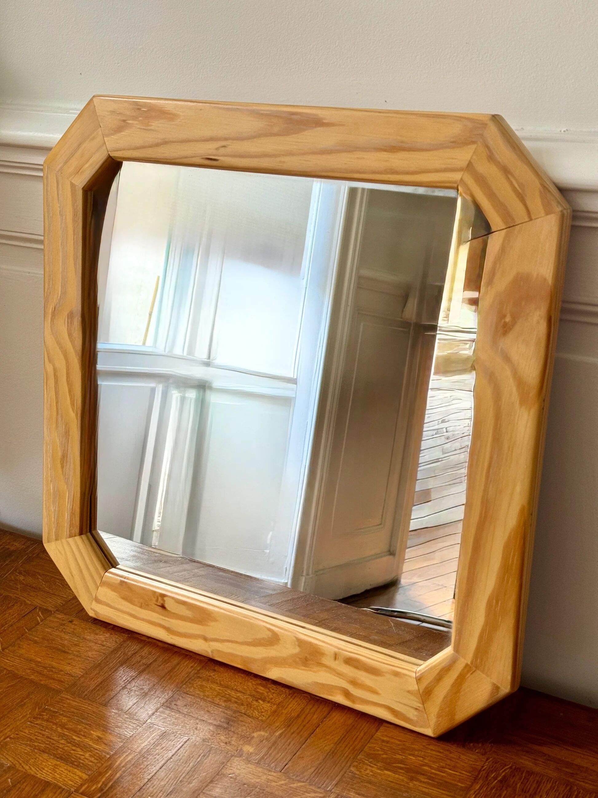 Octagonal mirror in light wood with grooves.