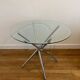 Round glass dining table with a chrome central base.