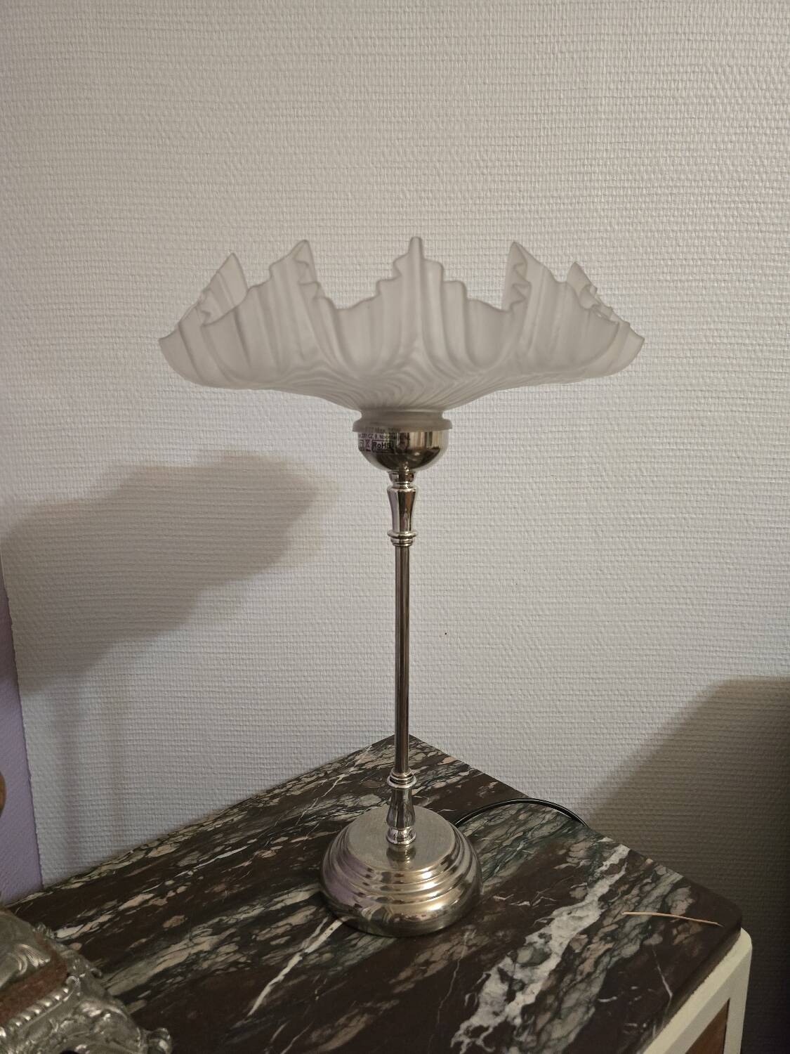 Table lamp with a silver base and a scalloped shade.