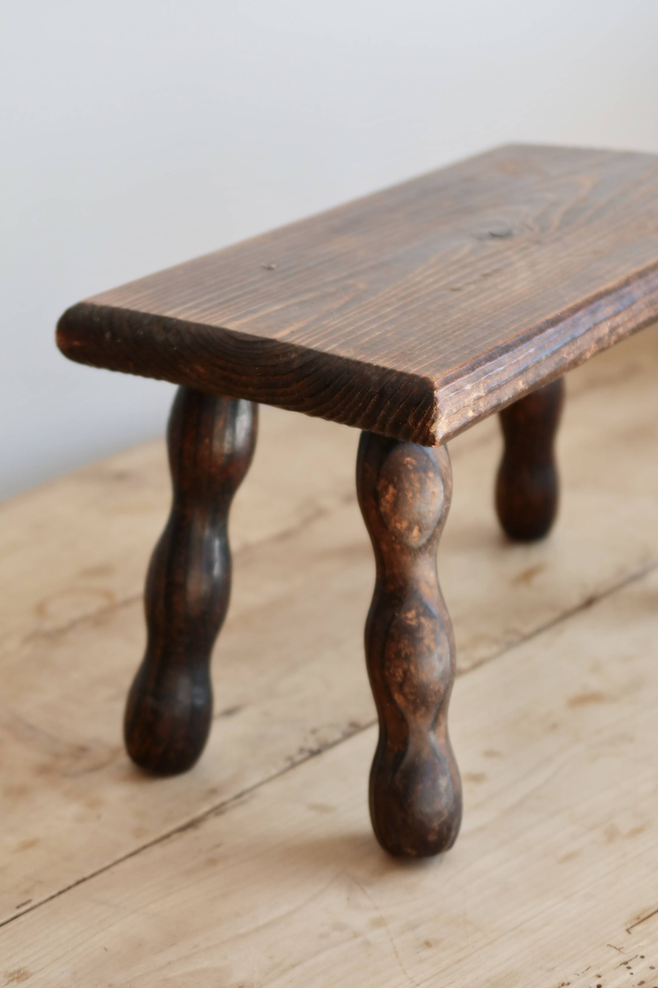 Vintage rectangular stool in dark wood with turned legs.