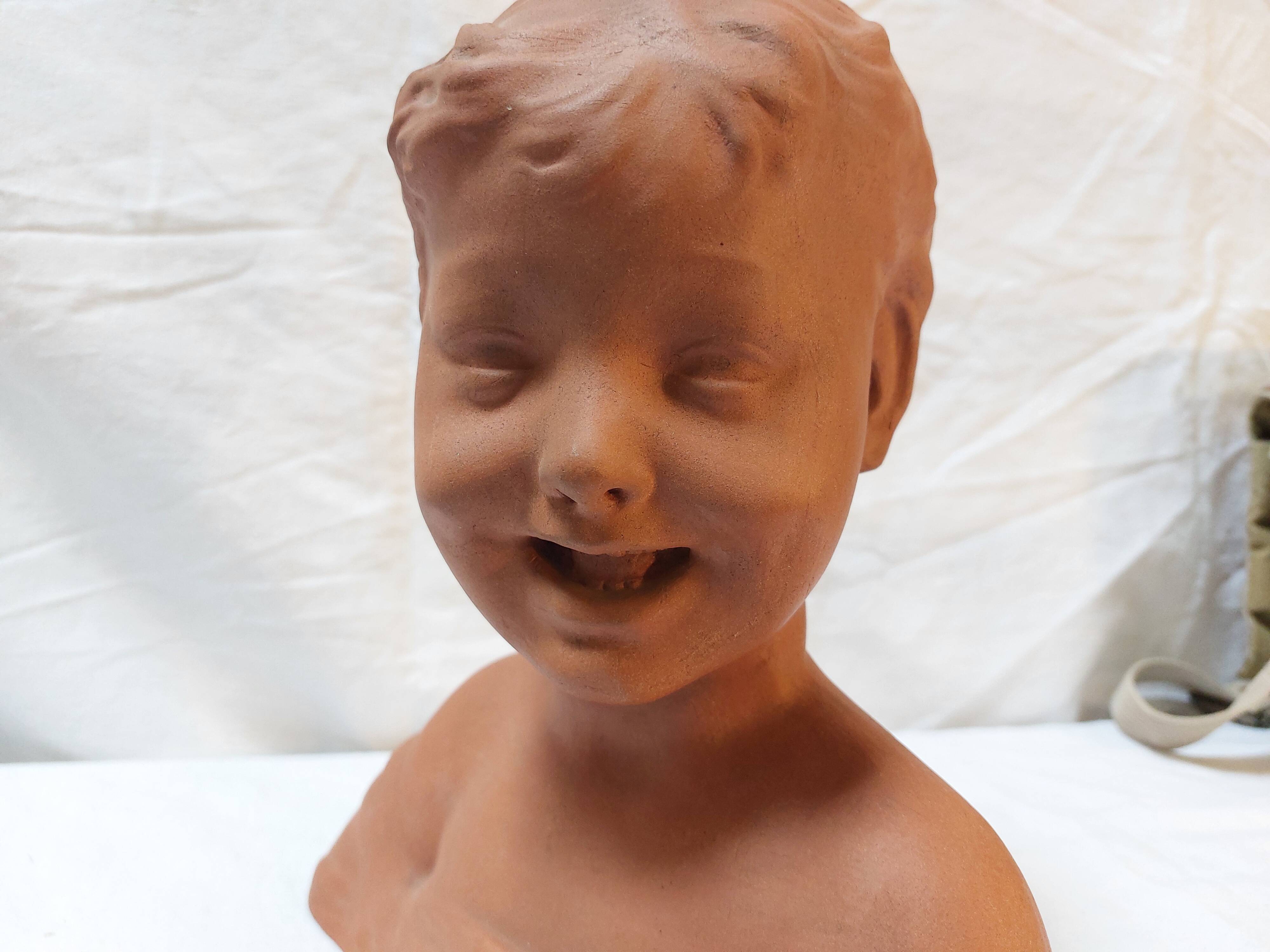 Terracotta bust of a smiling little boy.