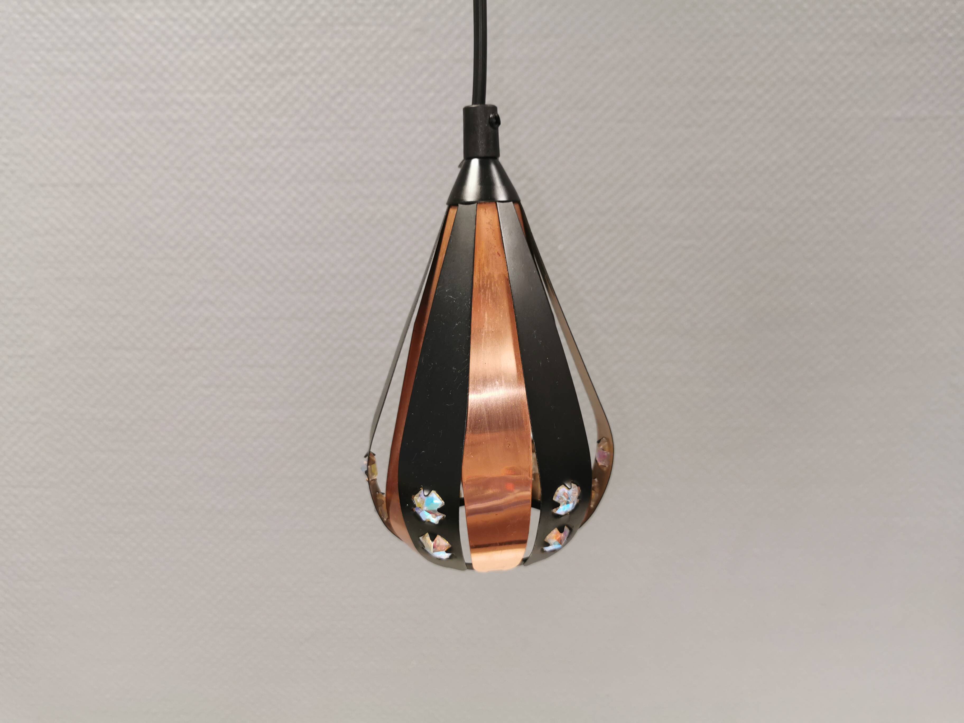 A teardrop-shaped pendant lamp made of copper, black metal, and prisms.