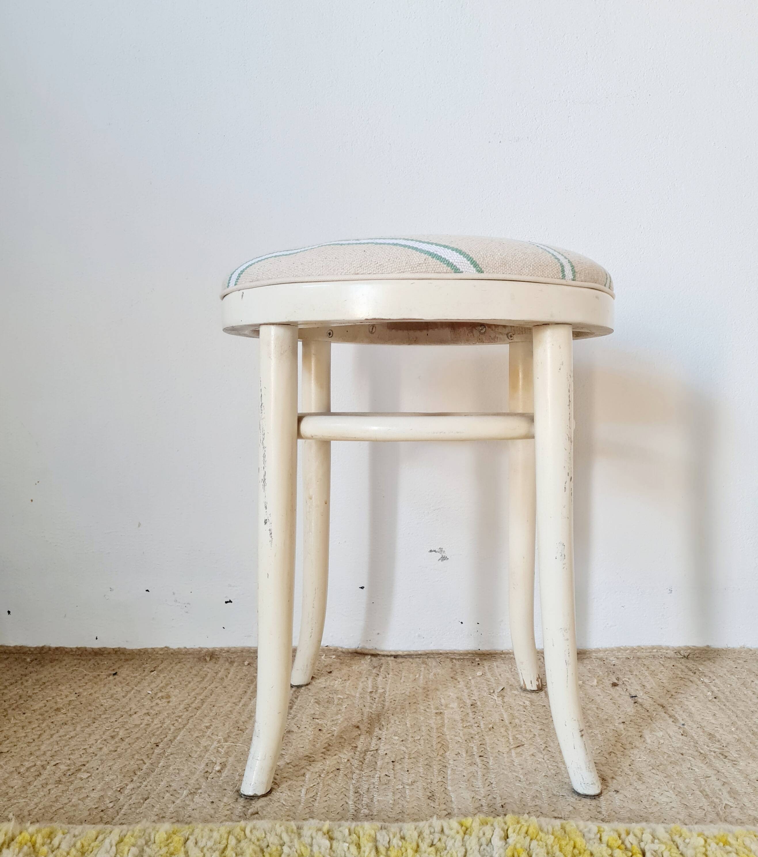 Antique stool with a wooden frame and a cream and green striped fabric seat.
