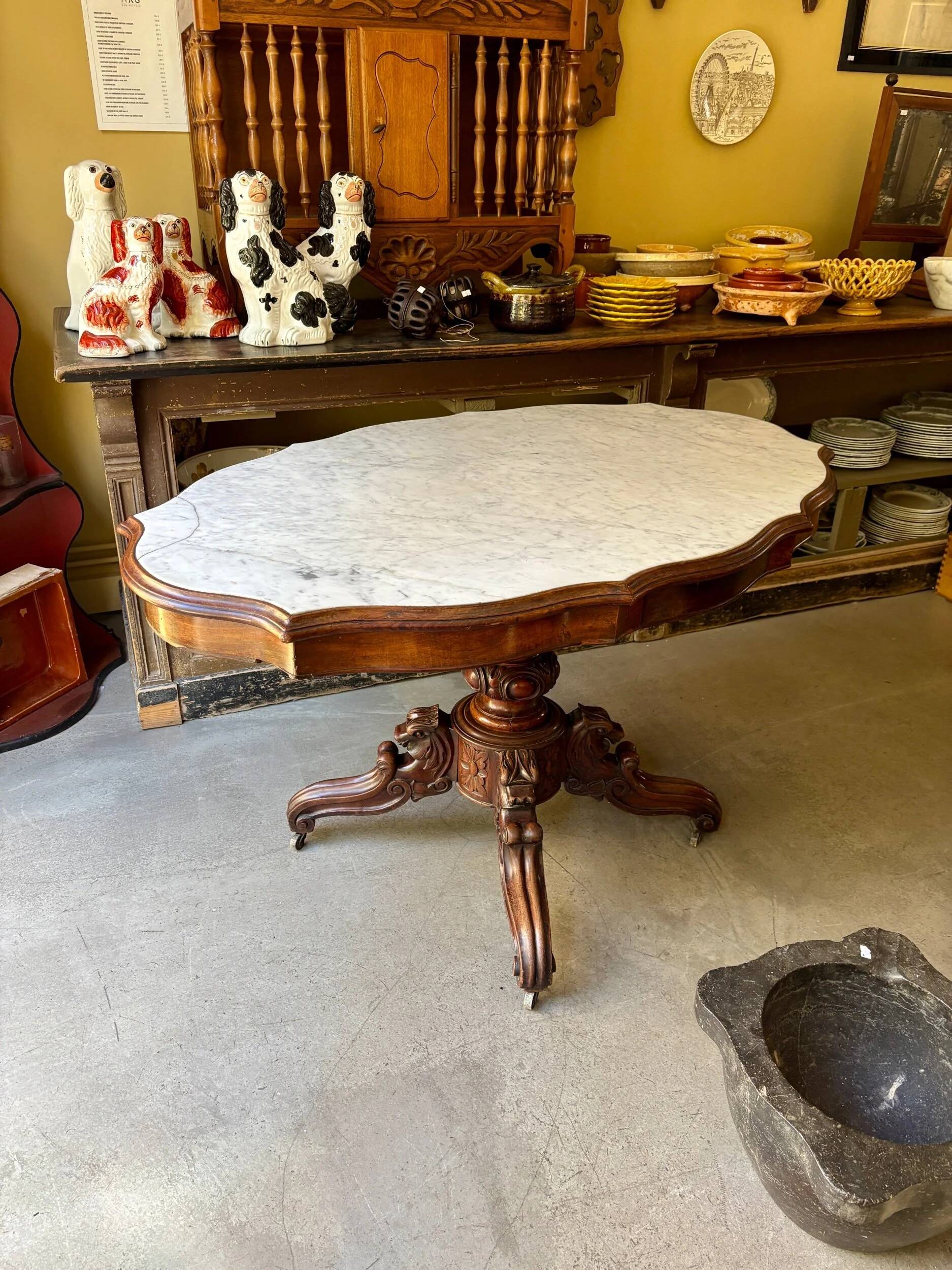 Table with a carved wooden frame and grey marble top on wheels, measuring 130 x 82 cm.