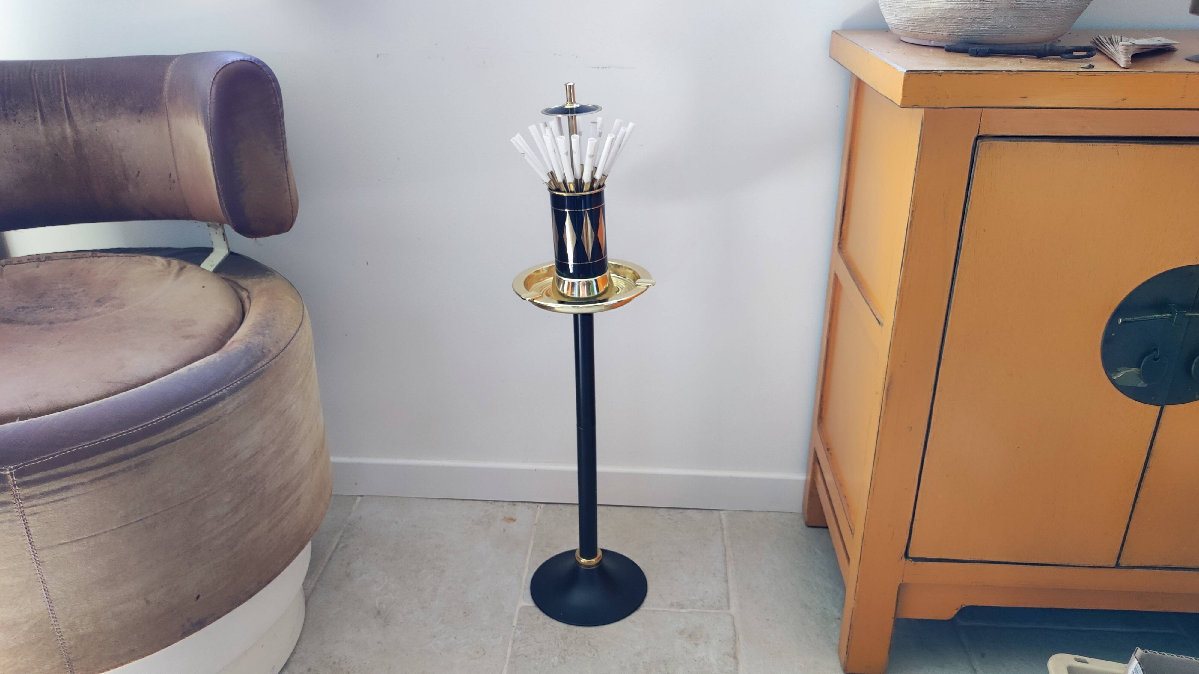 Vintage floor ashtray with a gold and black metal cigarette dispenser.