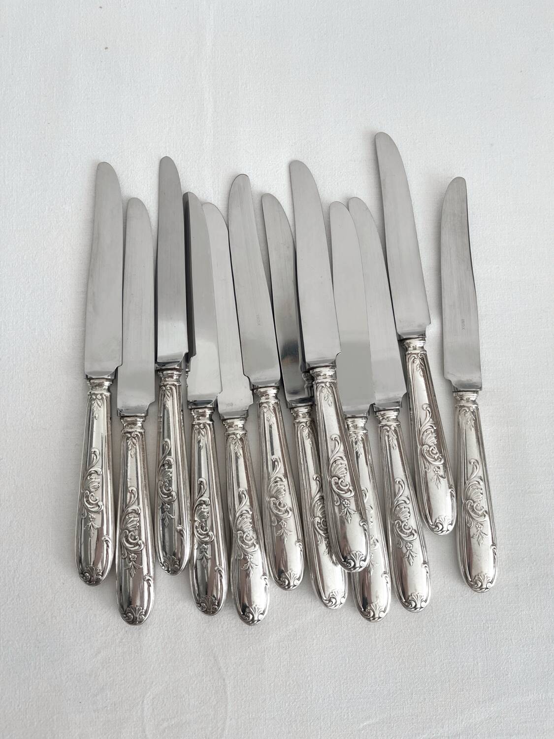 12 antique silver-plated knives with acanthus shell decoration and stainless steel blades.