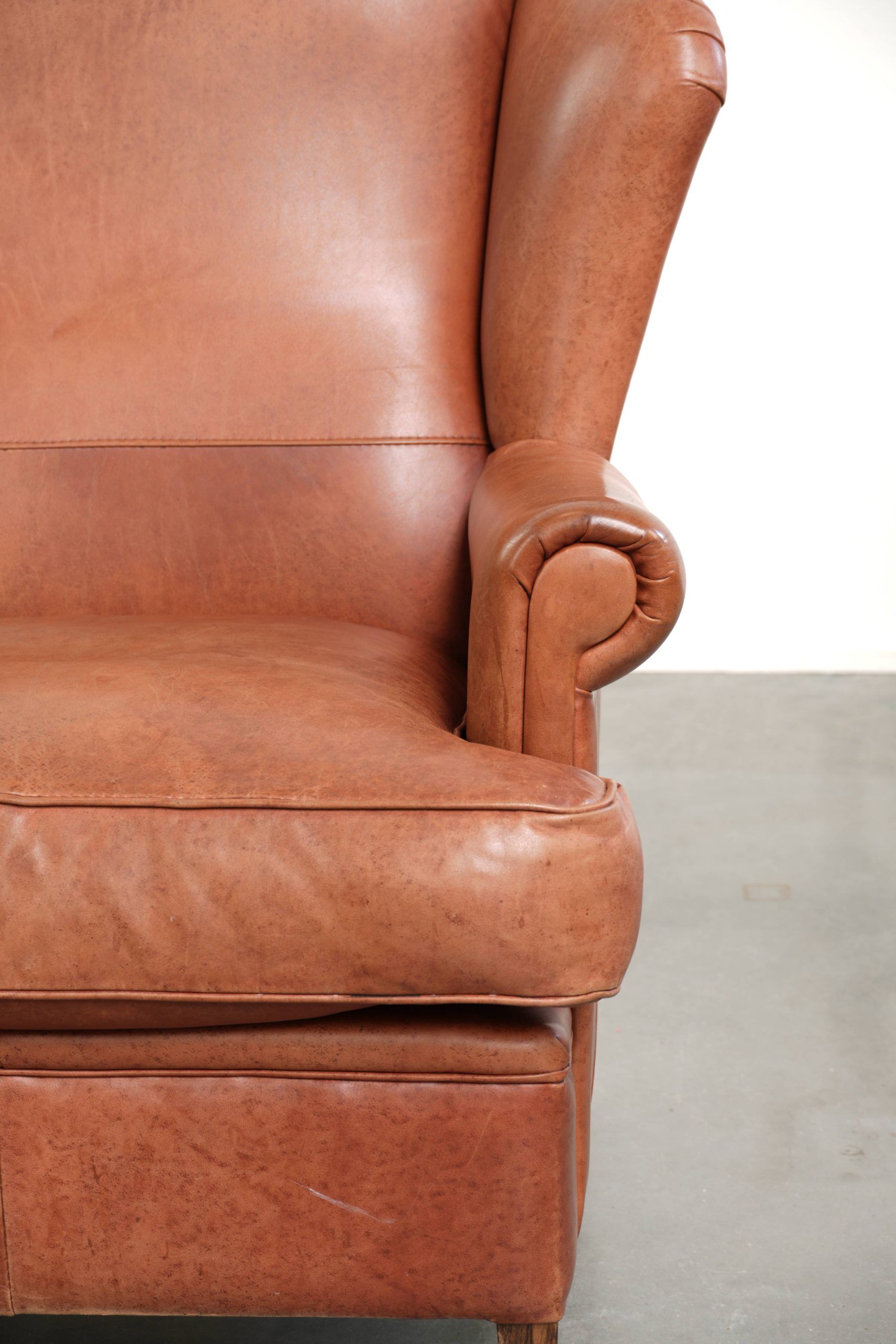 Light cognac-coloured cow leather wingback armchair with matching piping