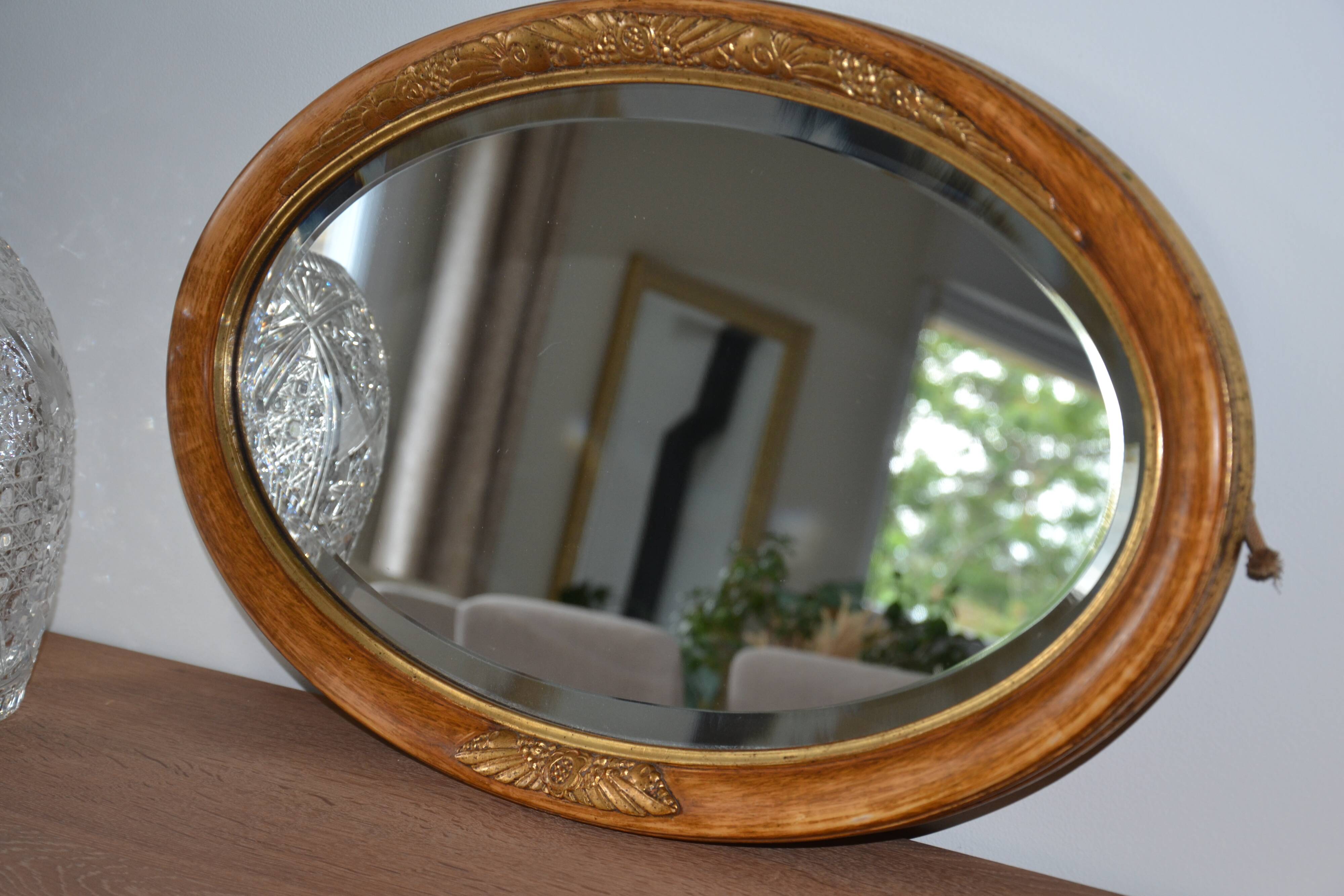 Old oval beveled wooden mirror, partly gilded and carved