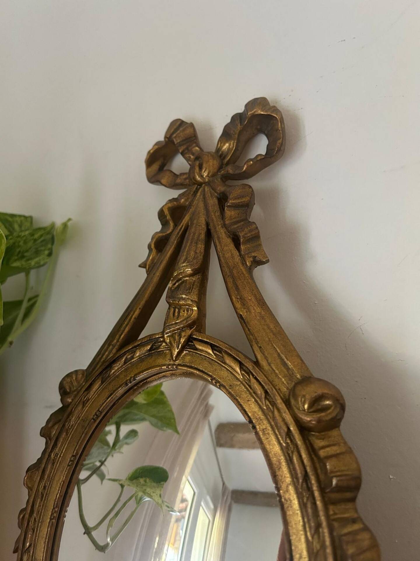 Oval convex witch mirror with golden ribbon mouldings.