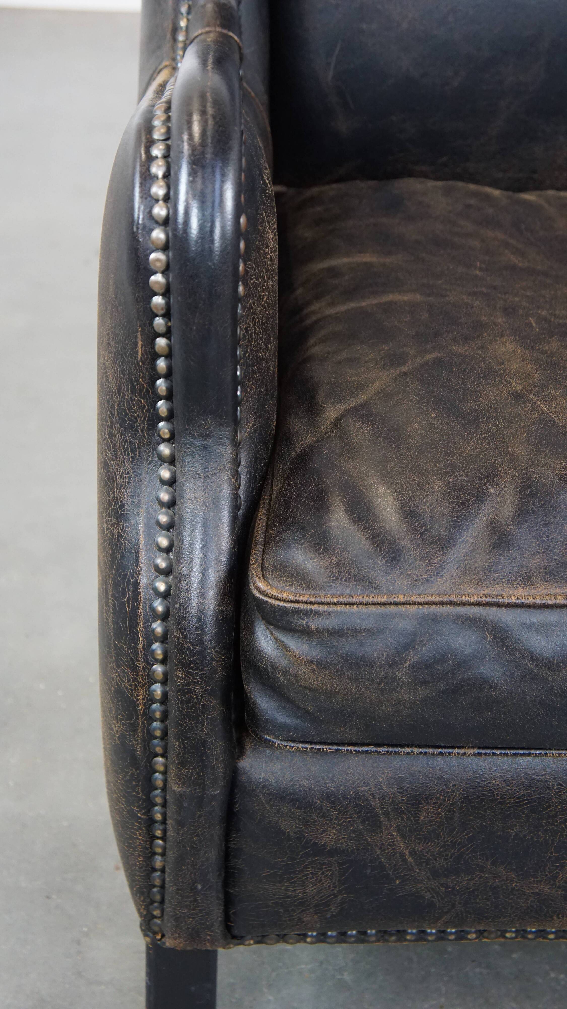 Black cow leather armchair in industrial style finished with decorative nails
