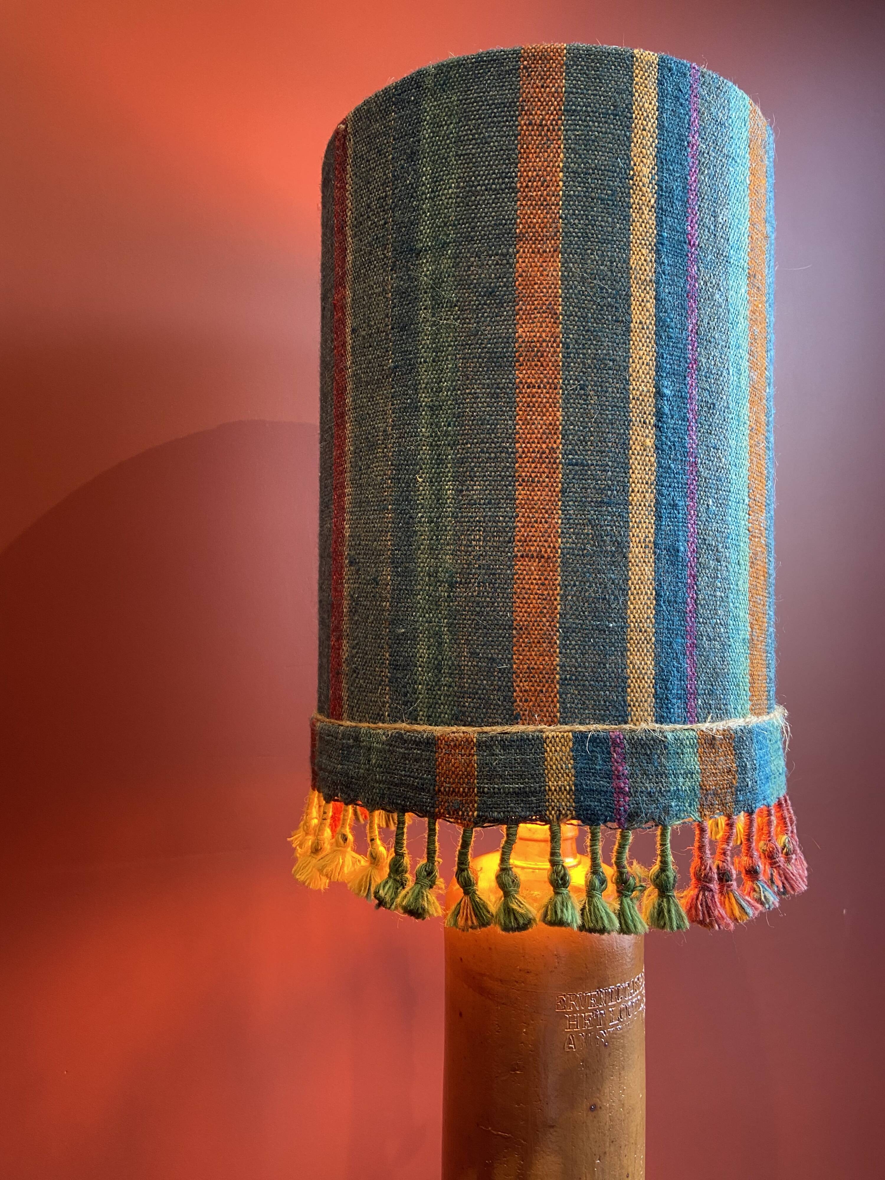 "Stoneware Bottle Lamp" with a multicoloured blue lampshade handwoven in India.