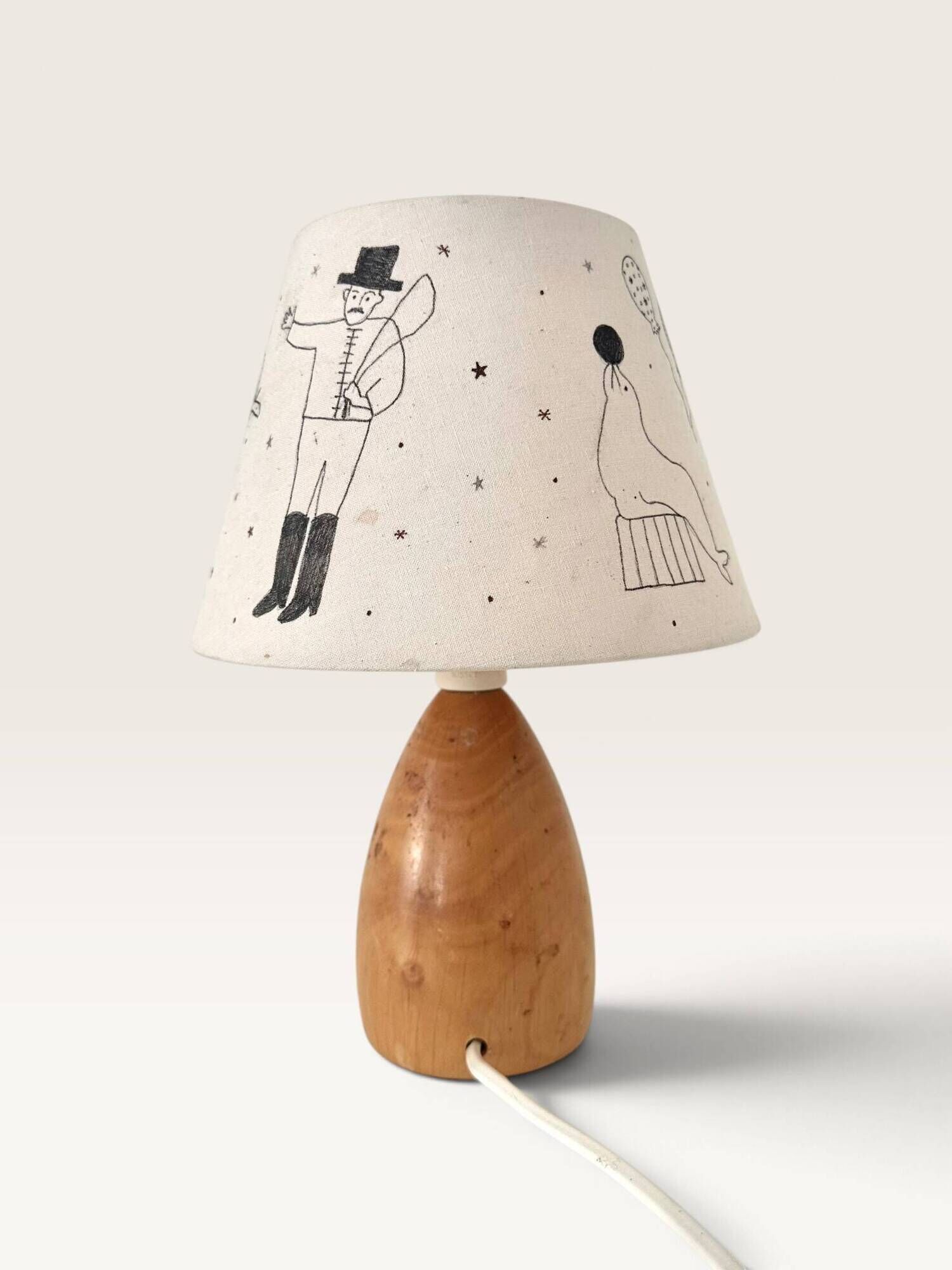 Wood-turned lamp with a hand-drawn lampshade, circus patterns.
