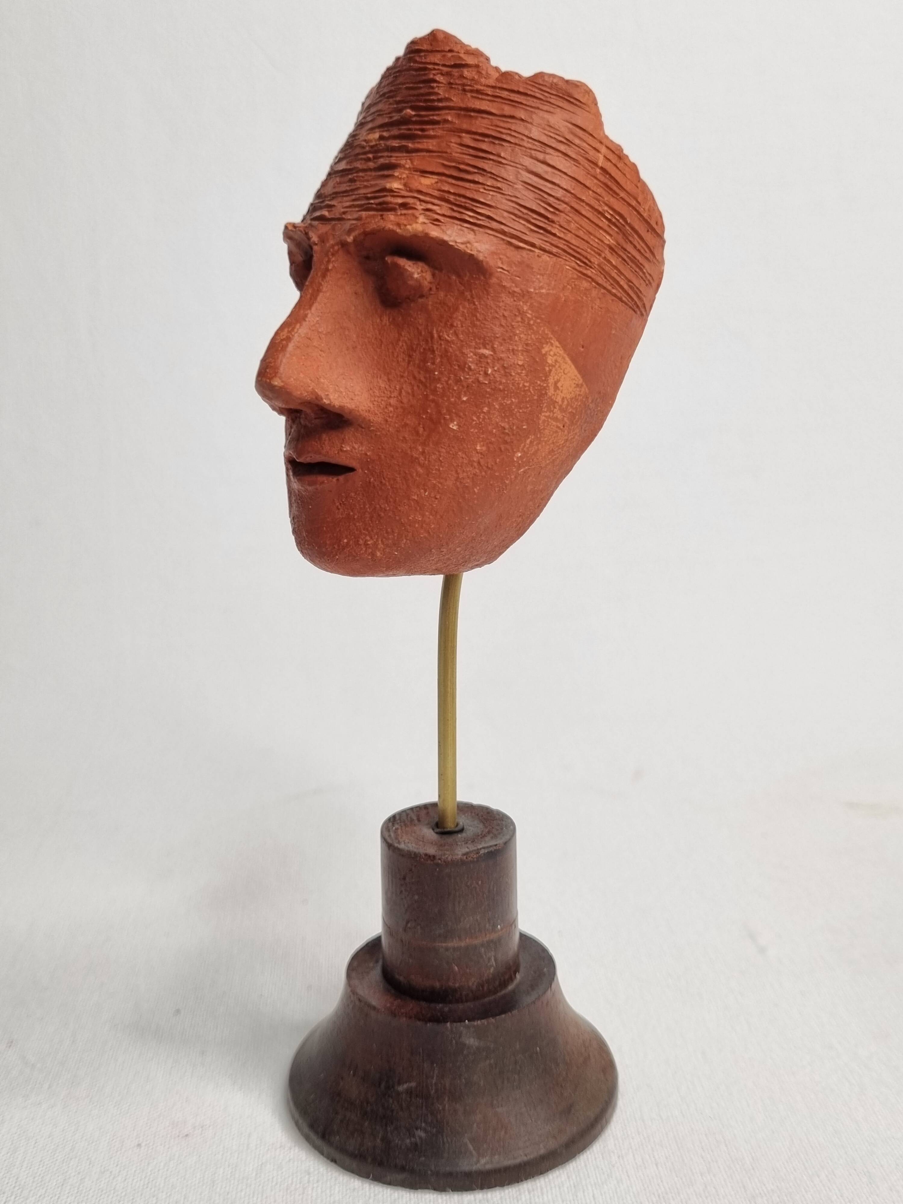 Stylized head in patinated ochre terracotta on a dark wooden base, 17 cm