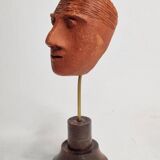 Stylized head in patinated ochre terracotta on a dark wooden base, 17 cm